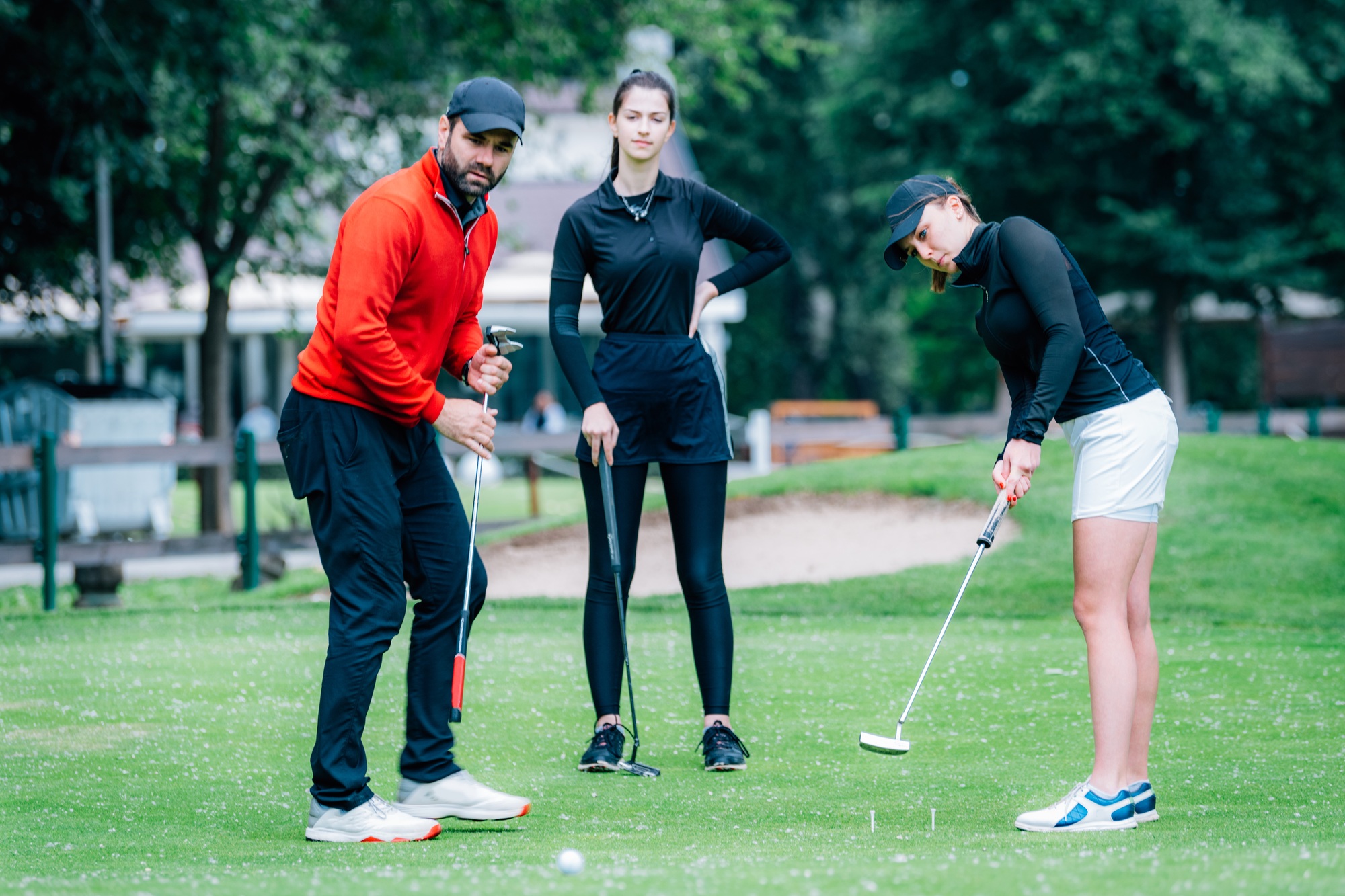 Golf putting lesson, two young female golfers practicing putting with golf instructor